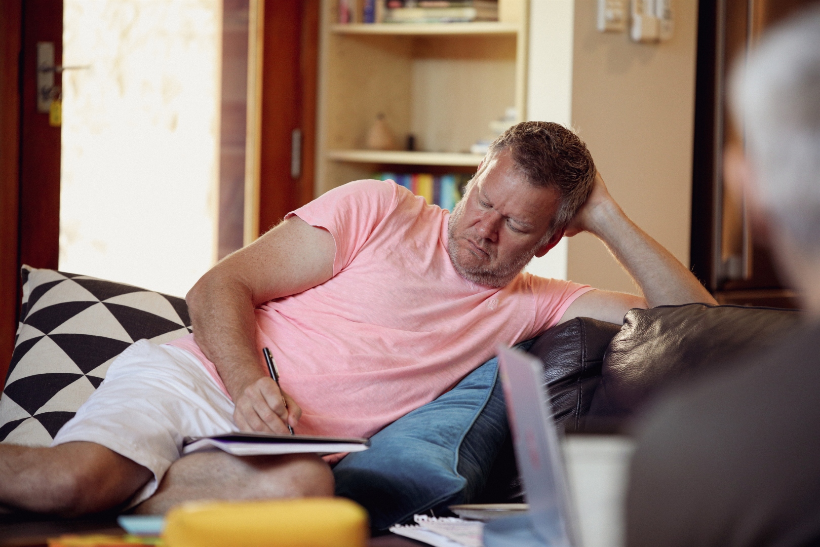 Craig Swanger writing in a notebook at home, deep in thought, in warm afternoon light