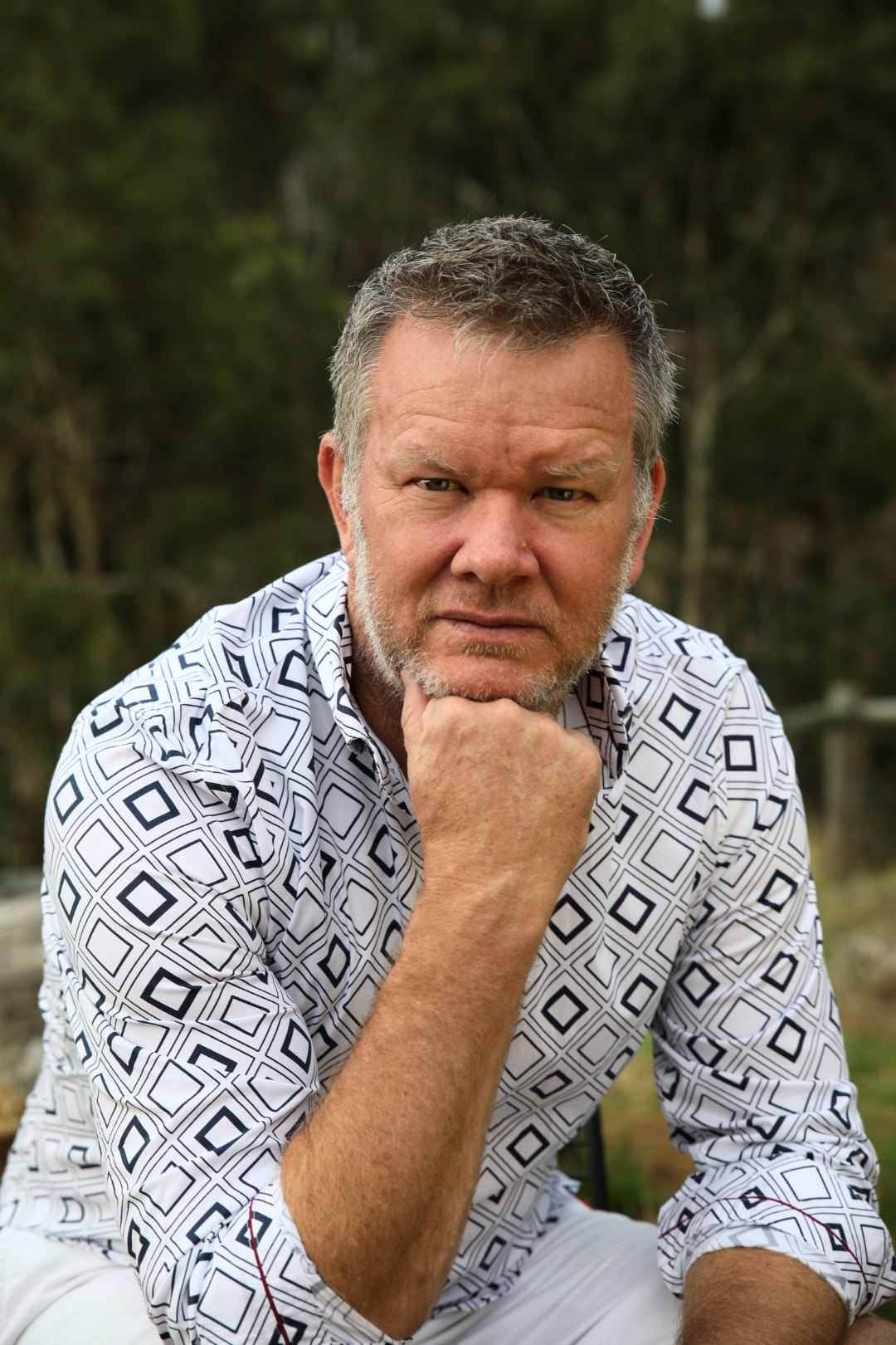 Craig Swanger seated outdoors, resting his chin on his hand in a reflective pose
