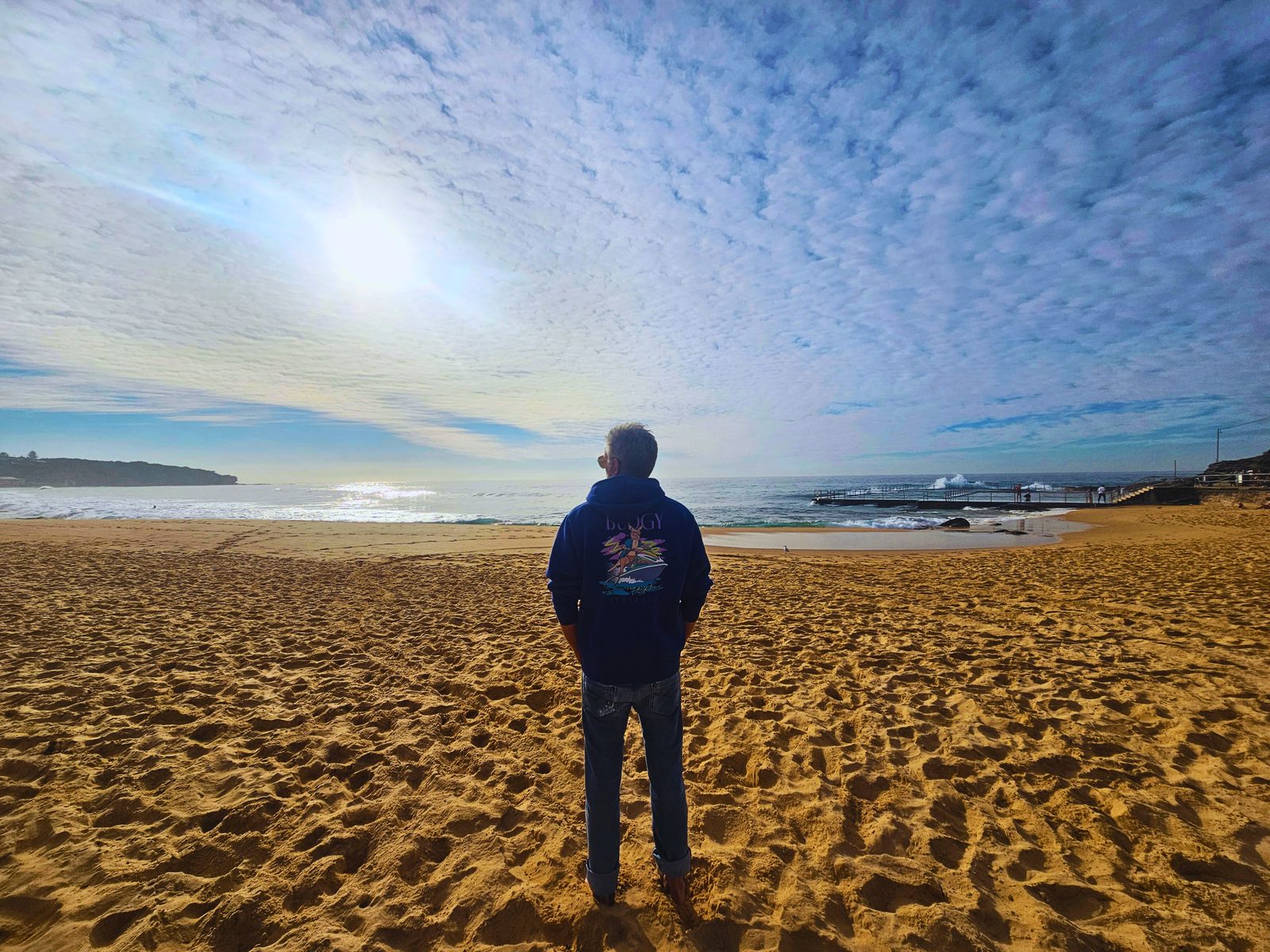 Craig Swanger standing on the beach at an ocean pool, looking out to the sea